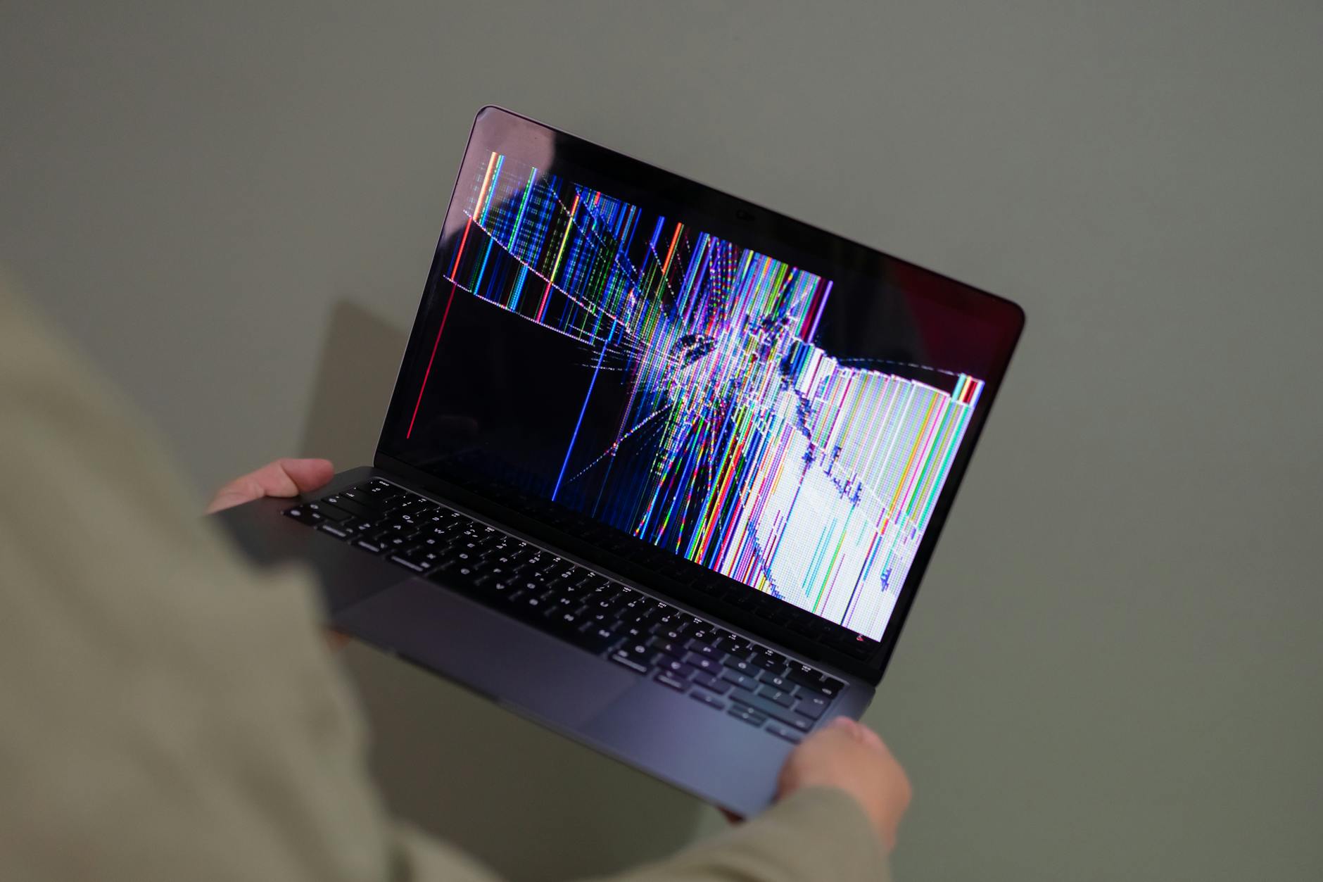 Osoba trzyma laptop z uszkodzonym, kolorowo „glitchującym” ekranem