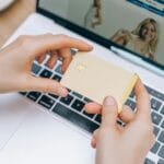 Dłonie trzymające kartę płatniczą nad laptopem podczas płatności online