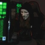 Haker w masce Guy Fawkesa przed monitorami w ciemnym pomieszczeniu